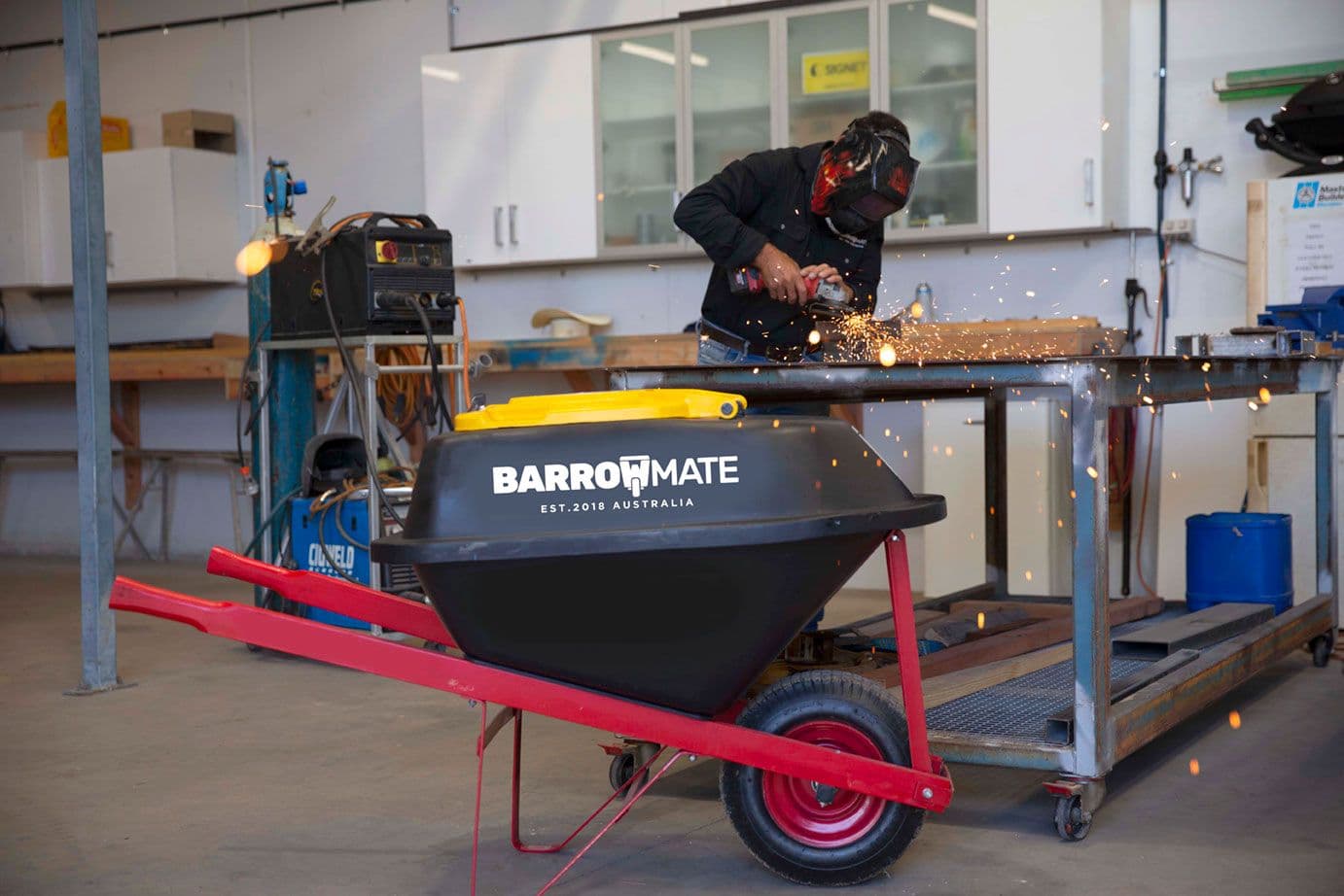 A Barrowmate on a wheelbarrow in a workshop while a welder works in the background